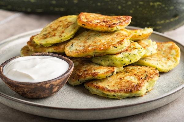 vegetable vegetarian zucchini pancakes with sour cream on a round plate and green zucchini - Оладьи с кабачком