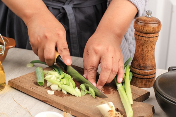 woman working in the kitchen chopping up the vegetables female slicing spring onions for salad close up chef cutting onions - Салат из кальмаров, квашеной капусты и лука