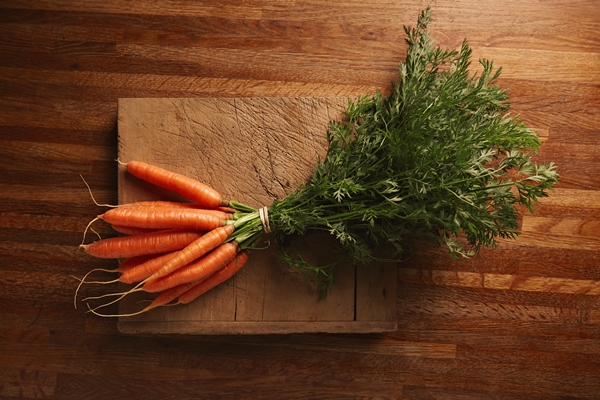 a bunch of fresh carrots on a weathered old cutting board with deep cuts on a beautiful wooden brown table top view - Салат с хреном, морковью и яблоками
