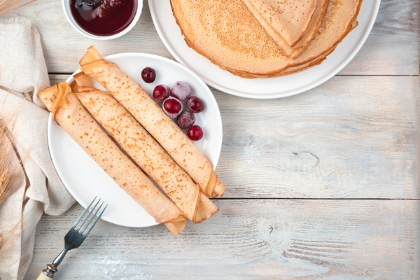 a portion of pancakes rolled into tubes with frozen berries on a light surface top view with space to copy the concept of cooking - Блинчики с яблоками
