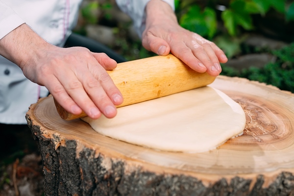 a restaurant chef in uniform rolls out dough on a stump in the woods - Плацинды постные