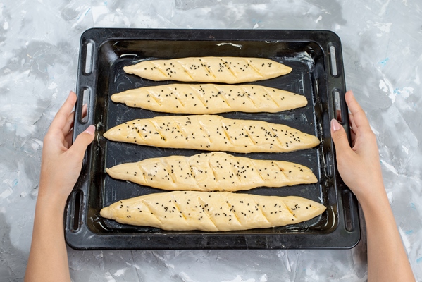a top view raw bread dough inside black tray with oil going into the oven on the light desk dough bread bun cooking - Штрудели с маком