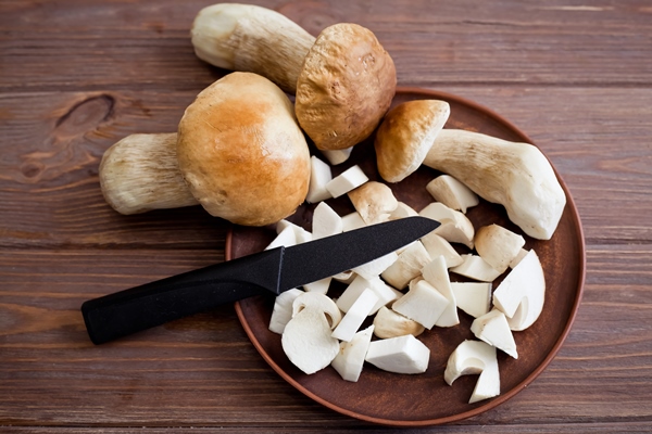 beautiful raw cutted and whole porcini mushrooms on a brown plate with a knife on a wooden table - Постная запеканка с картошкой и грибами