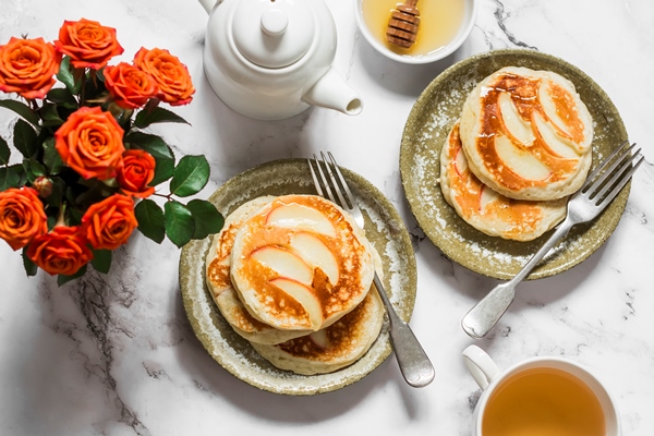 breakfast served pancakes with apples green tea a bouquet of roses on a light marble background top view - Оладьи постные с яблоками