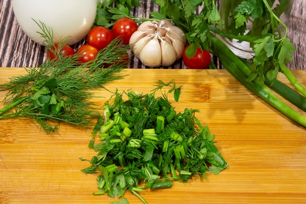bunches of green onions parsley and dill on a wooden chopping board next to tomatoes potatoes garlic and sour cream ingredients for salad - Тушёный картофель в томатном соусе