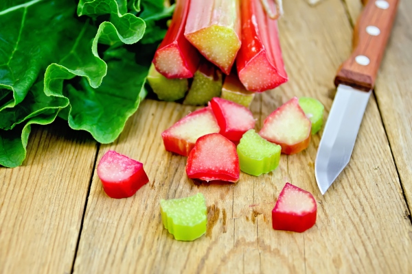 bundle of stalks of rhubarb cut pieces of rhubarb with a leaf and a knife on a wooden board - Маседуан из ревеня