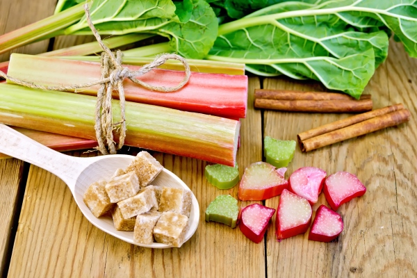 bundle of stalks rhubarb cut pieces of rhubarb with a sheet and a knife a spoon of sugar cubes cinnamon on a wooden board - Маседуан из ревеня