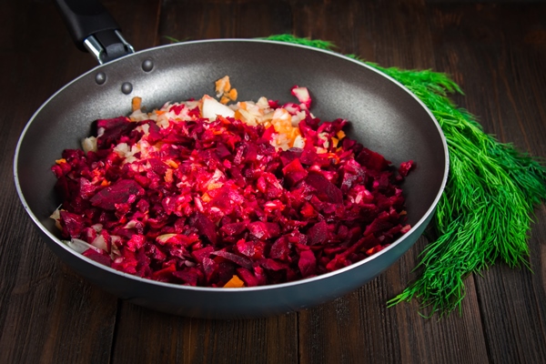 carrots beets and onions in a frying pan around dill on a brown wooden background - Свекольная икра