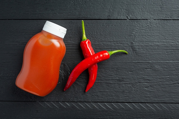 chili sauce in bottle and peppers on dark wooden surface - Рагу из картофеля с красным сладким перцем и капустой