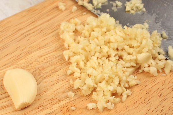 chopping white garlic on wooden chopping board - Постный суп из консервов