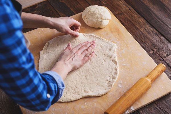 close up of female hands rolling out ball of pizza dough cooking at home - Пирог морковный открытый