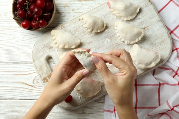 concept of cooking pierogi with cherry on white wooden table - Вишнёвые вареники с сиропом