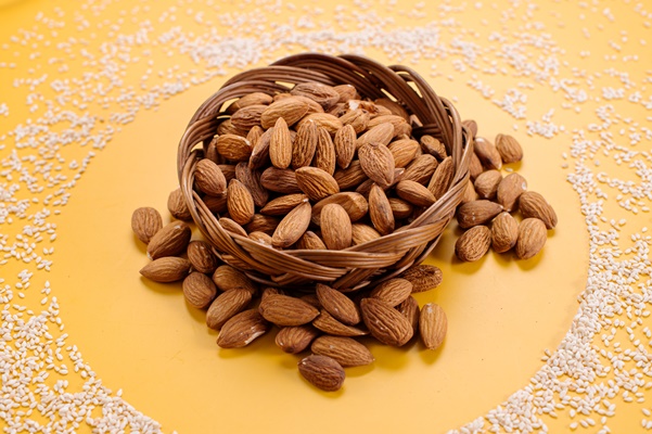 dried almonds in a basket on a background sprinkled with sesame seeds - Пирог сладкий с черносливом