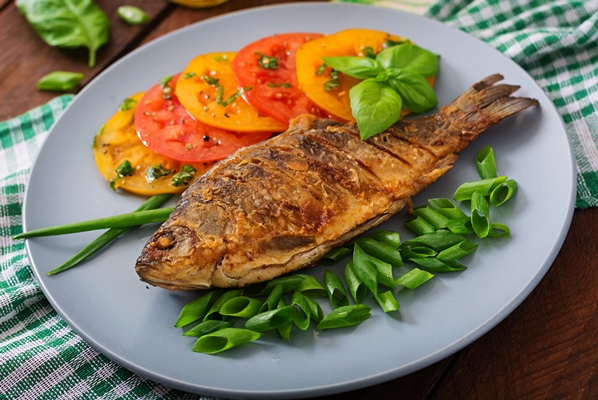 fried fish carp and fresh vegetable salad on wooden table - Карп жареный или печёный