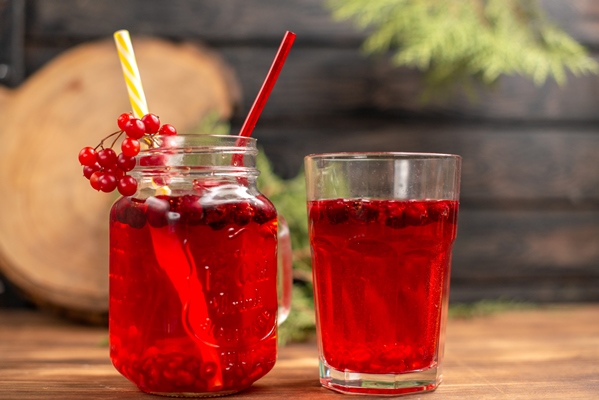 front view of natural organic fresh currant juice in a bottle served with tubes and in a glass on a wooden table - Напиток из калины