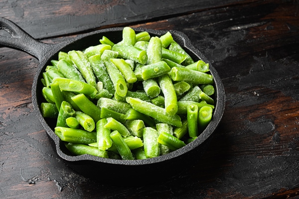 frozen cut green beans vegetable set in frying cast iron pan on old dark wooden table - Картофельный салат с фасолью