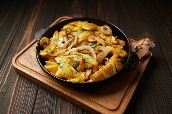 homemade fried potatoes with onions mushrooms and garlic in a frying pan on a wooden board - Картофель с грибами, постный стол