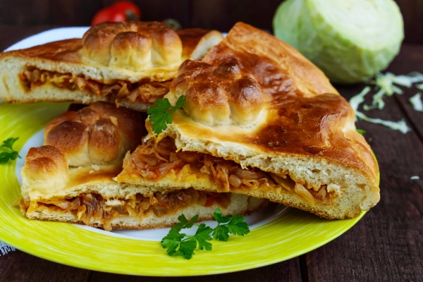 homemade pie with cabbage chopped pieces on a dark wooden background close up - Пирог со свежей капустой
