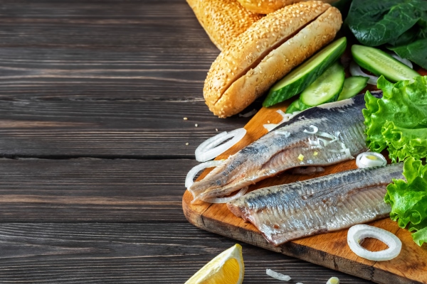 making herring fillet sandwich with onions cucumber and salad on a wooden board - Картофель ломтиками, запечённый с селёдкой