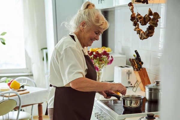 nice old woman in apron cooking dinner at home - Постная гречневая каша