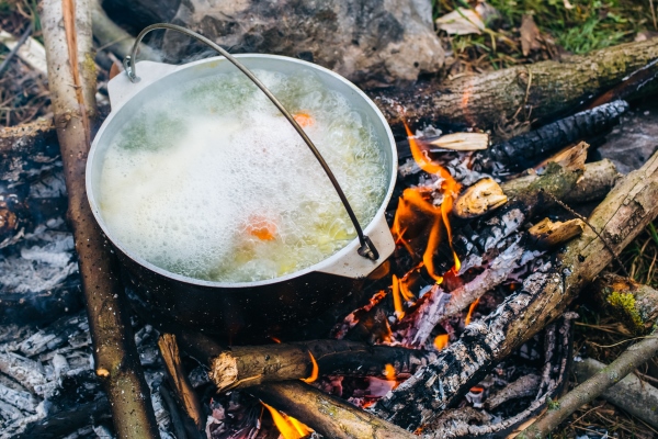 old vintage pot in black soot is standing on the open fire in the wood natural summer holidays photo fish broth cooked in the forest vegetarian carrots and potatoes vegetable soup - Форель варёная