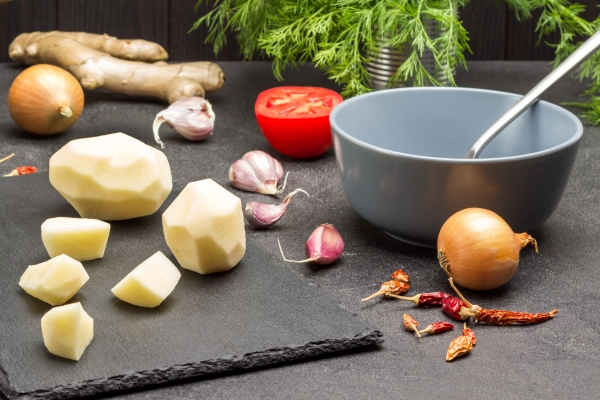 peeled potatoes and knife on cutting board parsley roots and beets in saucepan greens and vegetables on table black background - Картофель в кляре с грибным соусом