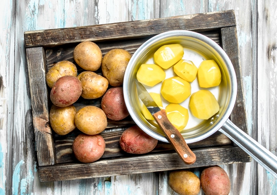peeled potatoes in a saucepan with unpeeled potatoes on tray with a knife on wooden - Картофельный холодец