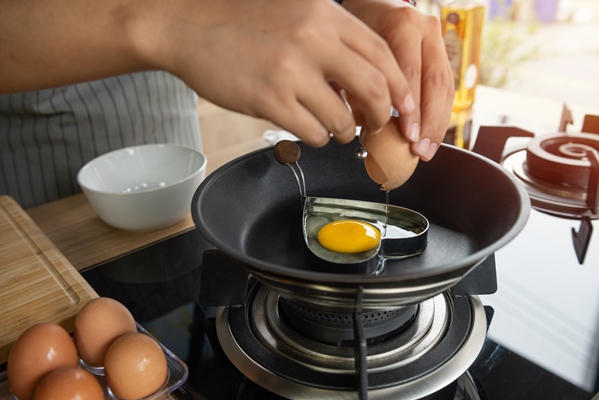 person breaking an egg into heart mold in a pan - Диетическая яичница