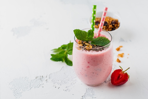 pink strawberries banana smoothie with granola and chia seeds in glass on light white concrete surface - Миндальный смузи