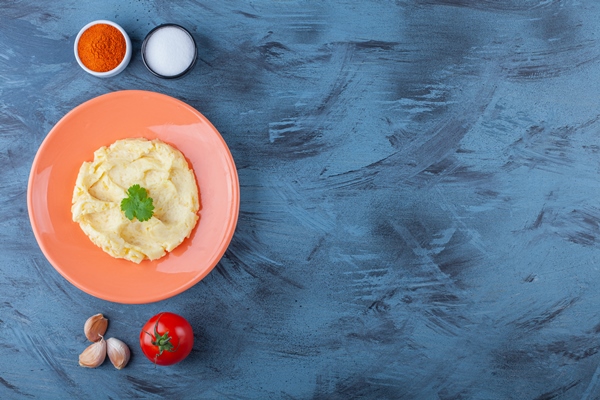 potatoes puree on a plate next to vegetables and spice bowls on the blue surface - Картофельный холодец