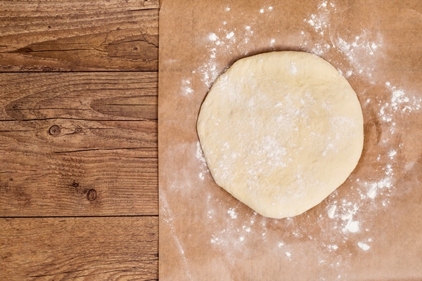 raw circular flatten dough on parchment paper over the wooden table - Слоёный сладкий русский пирог