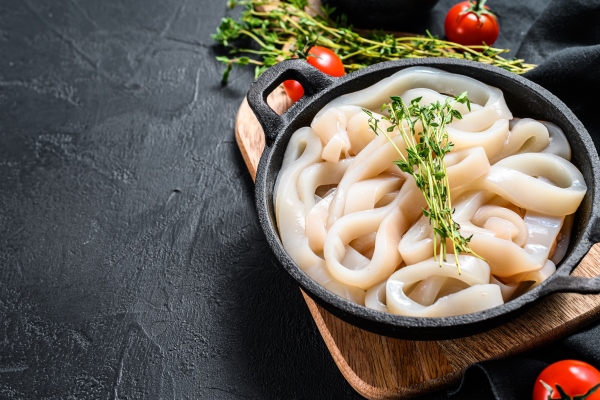 raw squid cut into rings in a frying pan black background top view copy space - Кальмары тушёные