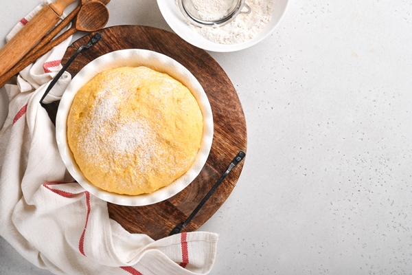 raw yeast dough with pumpkin in white bowl covered with towel on the floured kitchen table recipe idea concept home baking bread buns or cinnabon or making dough - Постный именинный крендель