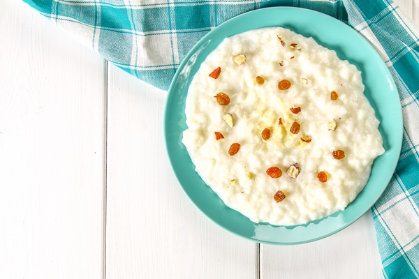 rice milk porridge with nuts and raisins in a blue dish on a white wooden table - Рисовая каша на воде