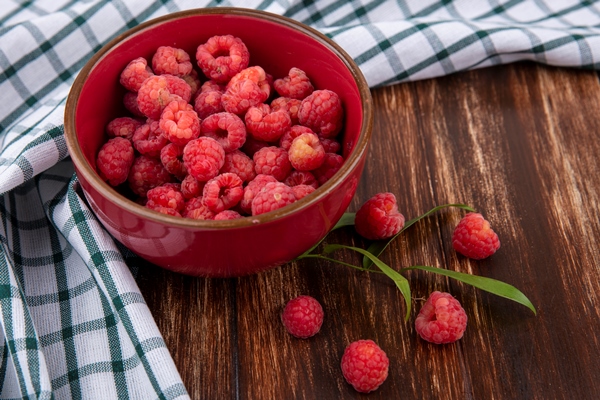 side view of raspberries in bowl on plaid cloth and leaves on wood - Квас из малинового сока