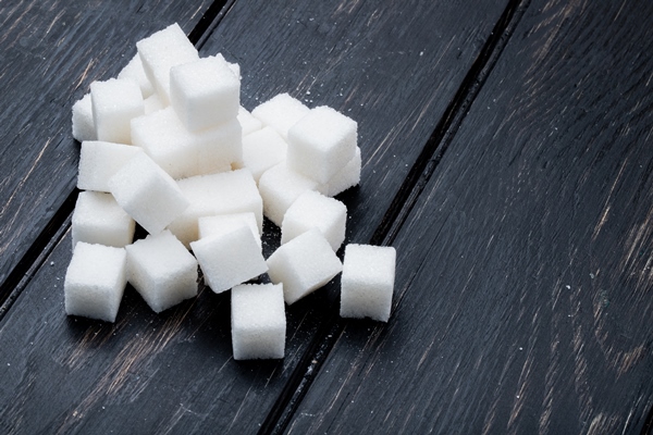side view of sugar cubes arranged on black wooden background with copy space - Напиток из шиповника