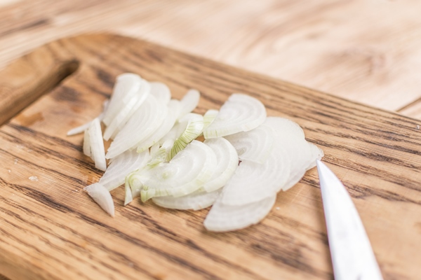 sliced onions with half rings on a wooden chopping board on a wooden background - Грибная подливка