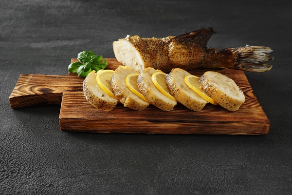 stuffed pike cut into round slices on a chopping board with lemon and basil leaf and the rest - Щука по-еврейски