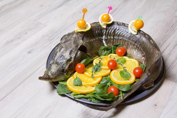 sturgeon with oranges spinach cherry tomatoes and physalis baked whole selective focus - Осетрина варёная с хреном и уксусом