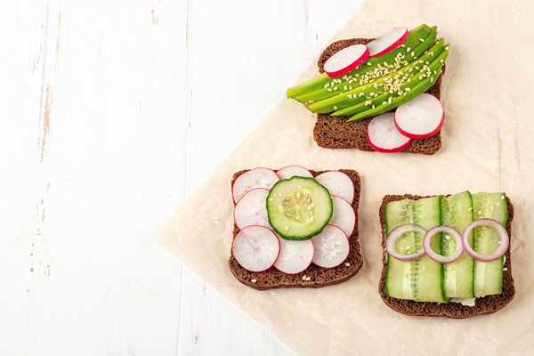 superfood open vegetarian sandwich with different toppings avocado cucumber radish on a paper on white background healthy eating organic and veggie food - Витаминный перекус
