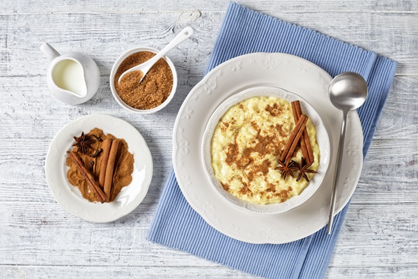 sweet rice pudding with cinnamon and anise star in a white bowl with spoon on a white wooden table with ingredients flat lay - Пудинг из риса с яблоками и вареньем