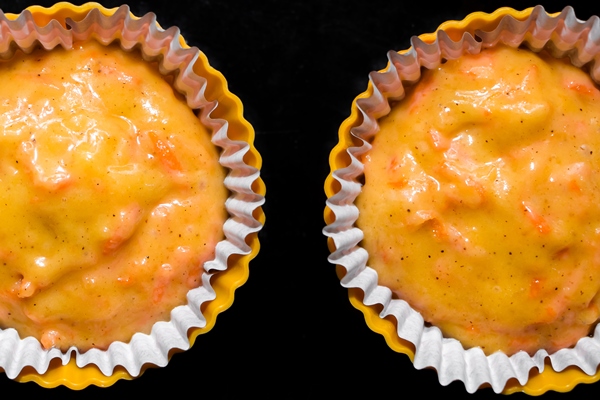 the process of making carrot muffins dough for cakes in paper molds on a black background - Пряники из морковного жмыха