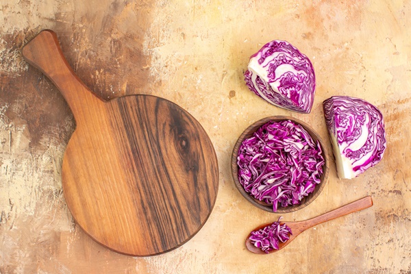 top view concept with a bowl of chopped red cabbage and a cuttung board for making beet salad on a wooden background with copy place - Свежая шинкованная капуста