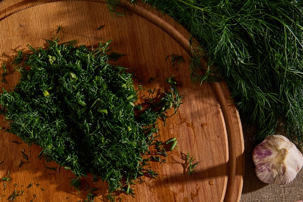 top view of a bunch of fresh moist dill on a linen tablecloth and garlic next to a wooden cutting board with a kitchen knife and chopped dill seasonal greens food background flat lay - Соус Тартар