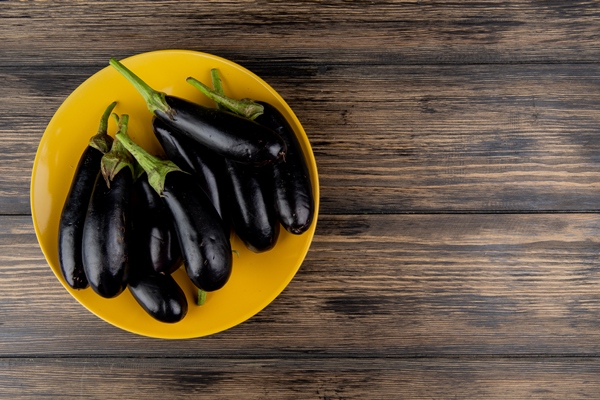top view of eggplants in plate on left side and wooden background with copy space - Свекольный салат