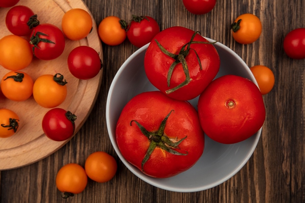 top view of fresh three large red tomatoes on a bowl with cherry tomatoes isolated on a wooden kitchen board on a wooden surface - Томатно-чесночный соус