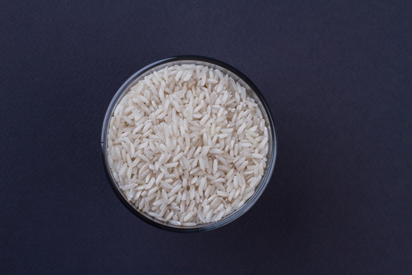 top view uncooked raw rice in a transparent glass cup dark blue background - Суп грибной с рисом, постный стол