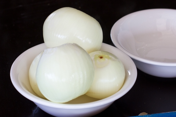 white peeled onion in a porcelain bowl on a blue wooden table on a black background - Котлеты постные из кальмаров