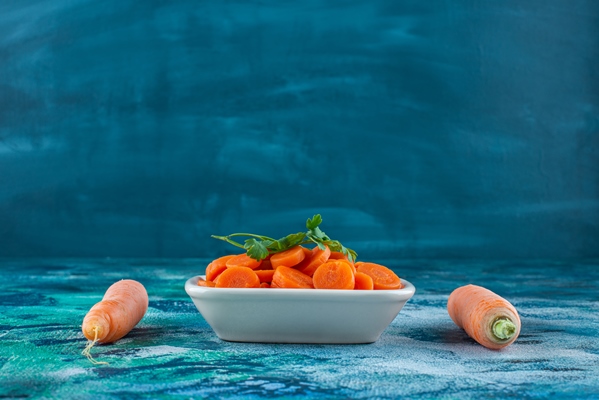 whole and slice carrots with parsley in a bowl on the blue table - Морковь тушёная постная