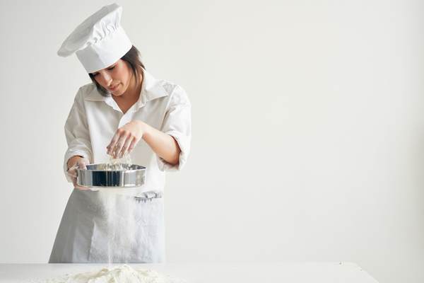 woman chef sifting flour on the table bakery cooking pastry - Булки заварные